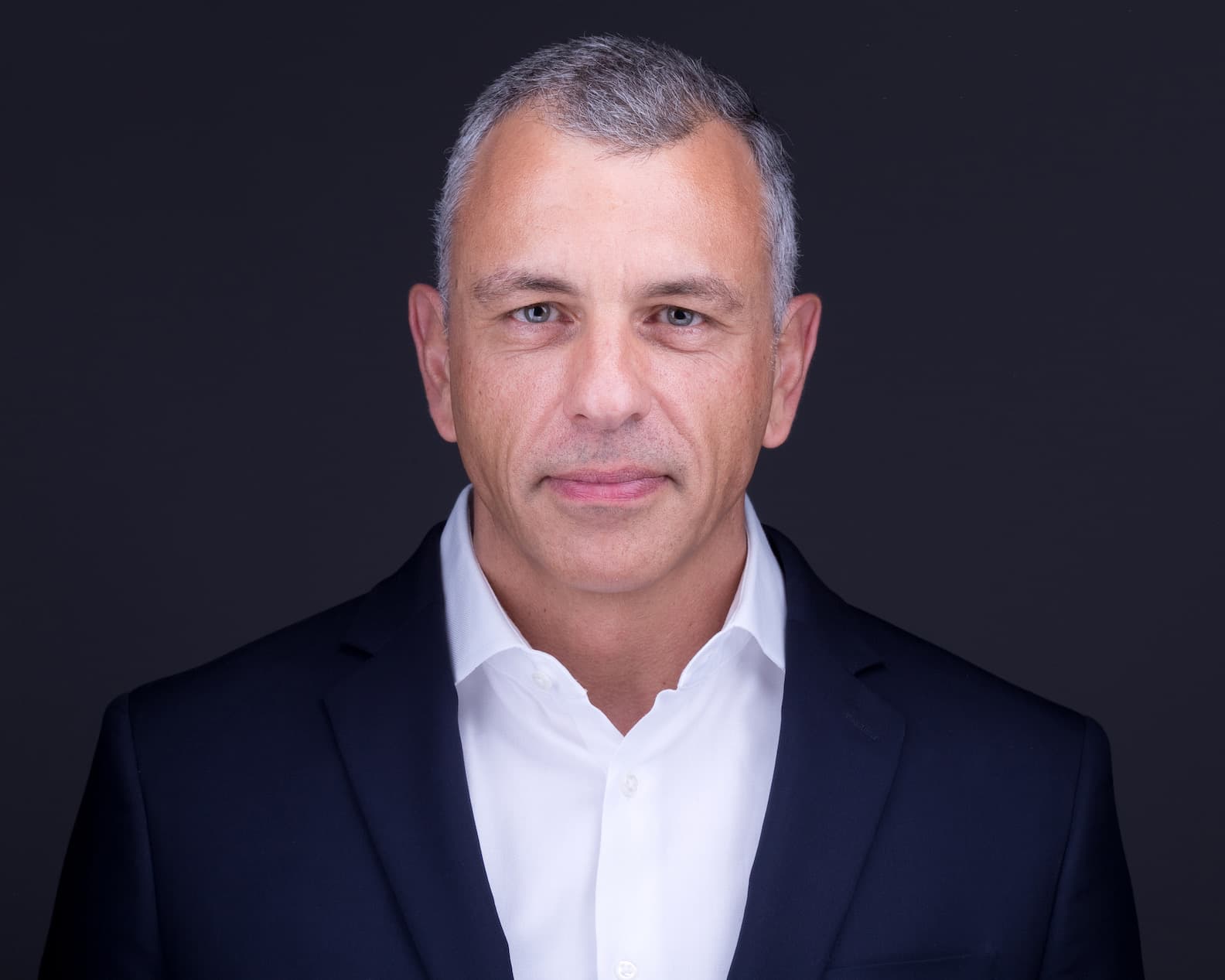 Professional headshot of a man with short gray hair in a suit and white shirt.